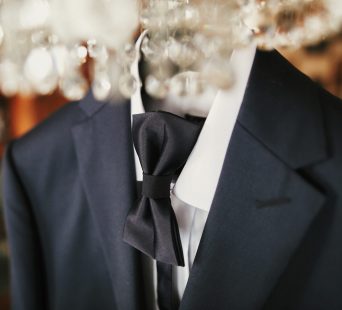 stylish black suit with white shirt and bow tie on hanger on luxury chandelier. morning preparations before wedding day. groom outfit